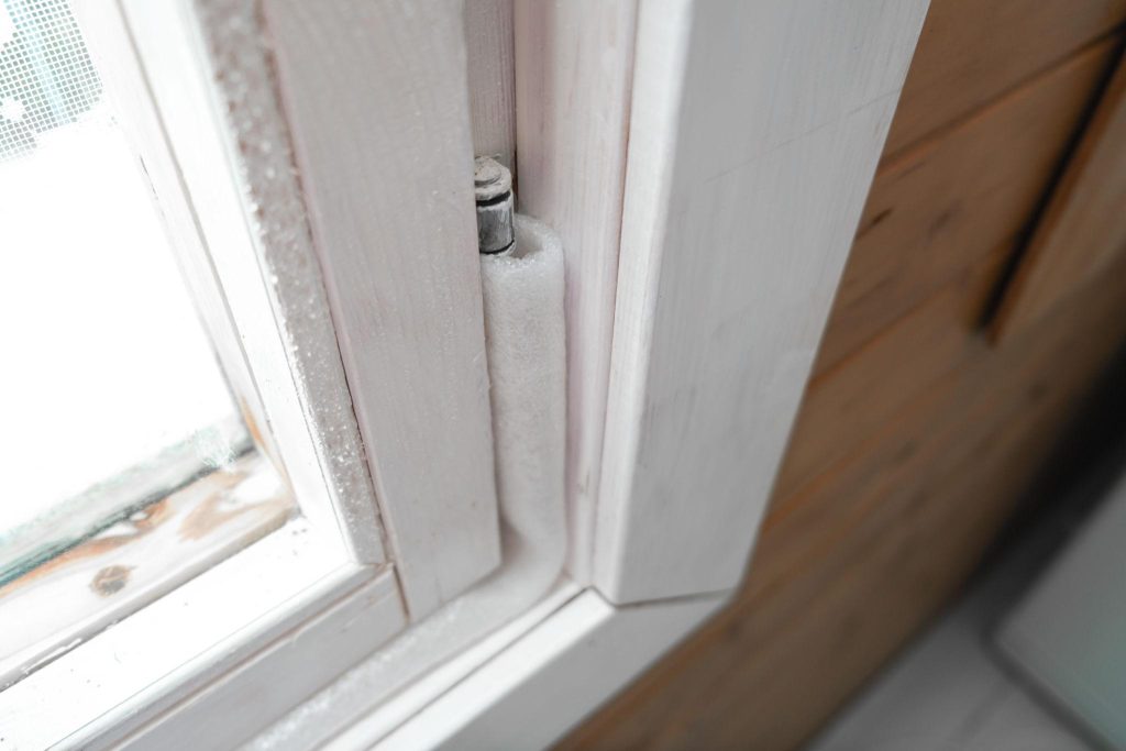 Frost forming along the interior hinge and frame of a residential window during freezing winter temperatures.