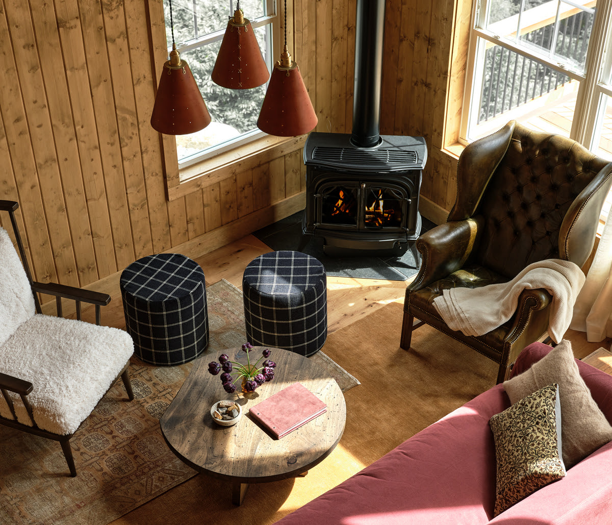 Sunlit Maine living room with wood stove, rustic wood walls, and cozy seating area in winter