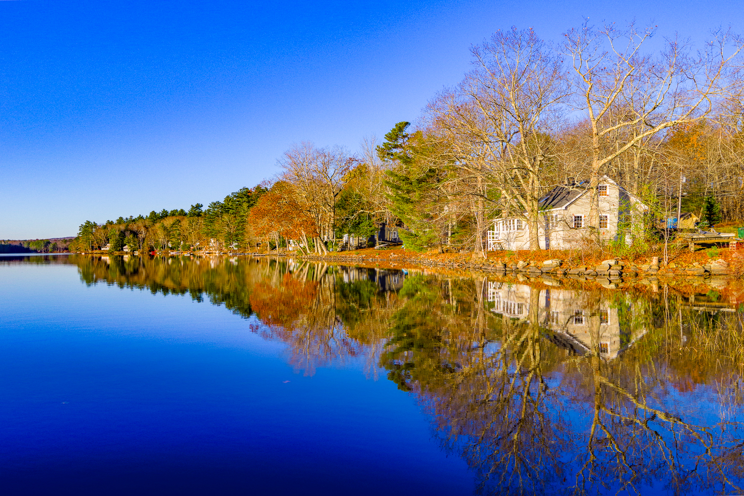 Waterfront home along a calm river in Lincolnville, Maine with fall foliage and reflection—Maine waterfront real estate and buying and selling homes in Maine.