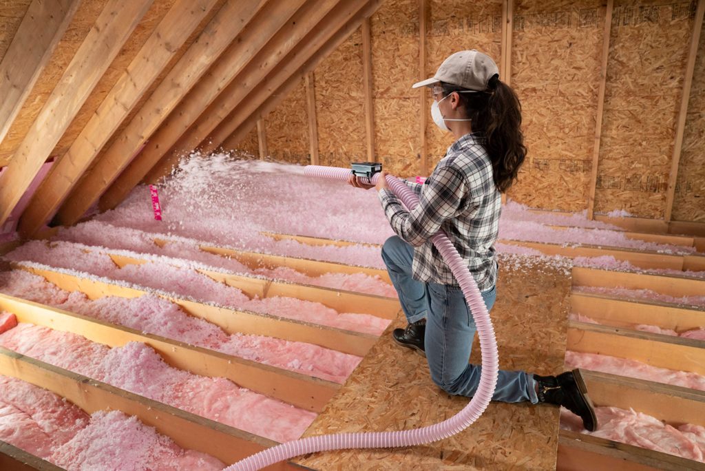 Worker installing blown-in insulation in attic space to improve energy efficiency during cold weather.