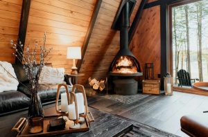 Warm wood-paneled Maine cabin interior with a modern wood-burning fireplace and large window overlooking snowy trees and water.