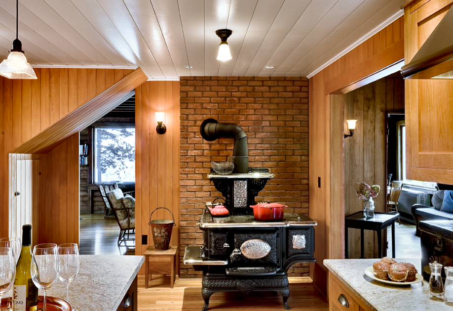 Traditional wood-burning stove set against brick wall in a warm, wood-paneled Maine kitchen interior.