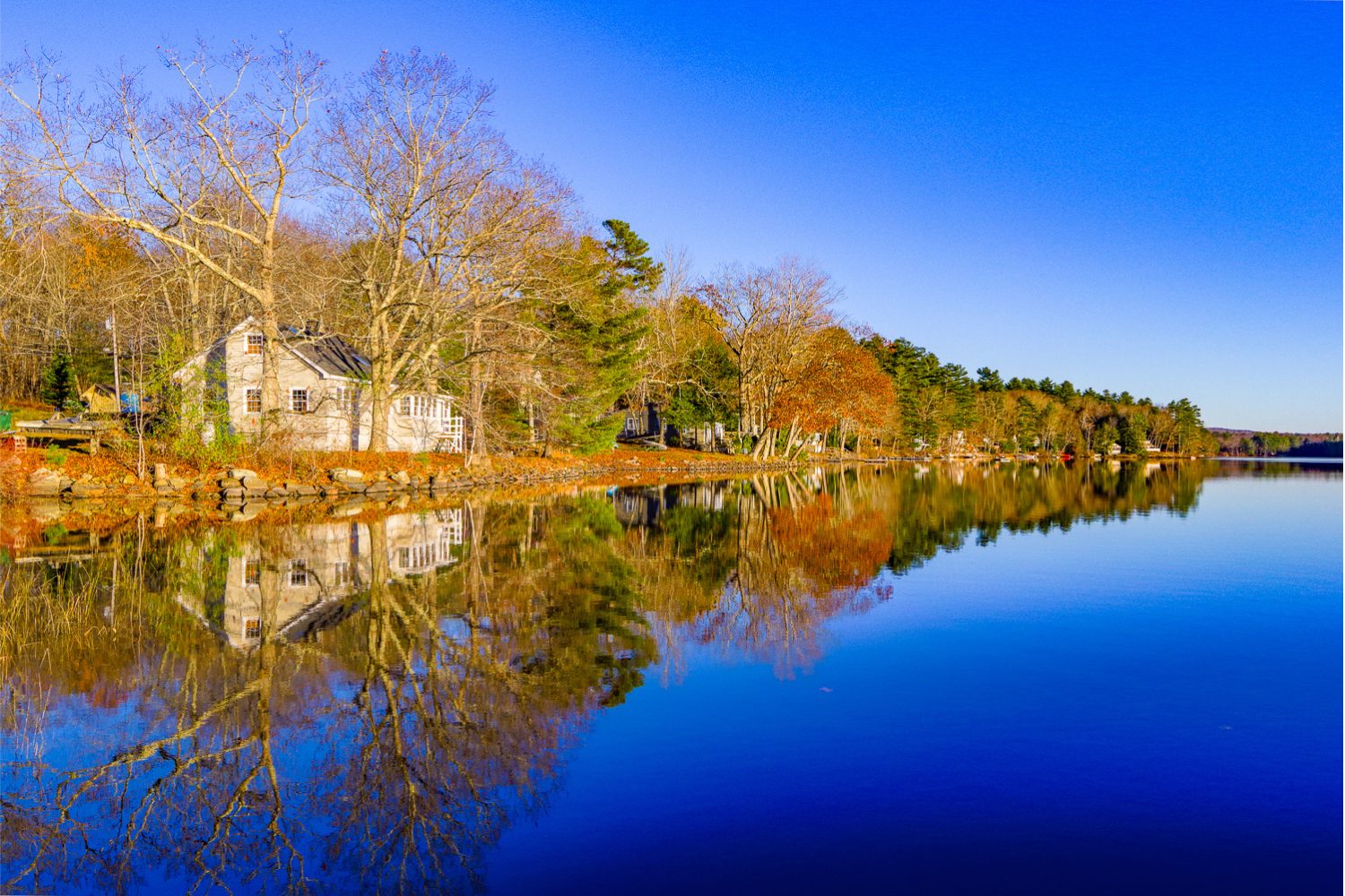 Waterfront homes and fall foliage in Lincolnville Maine reflected on calm water.