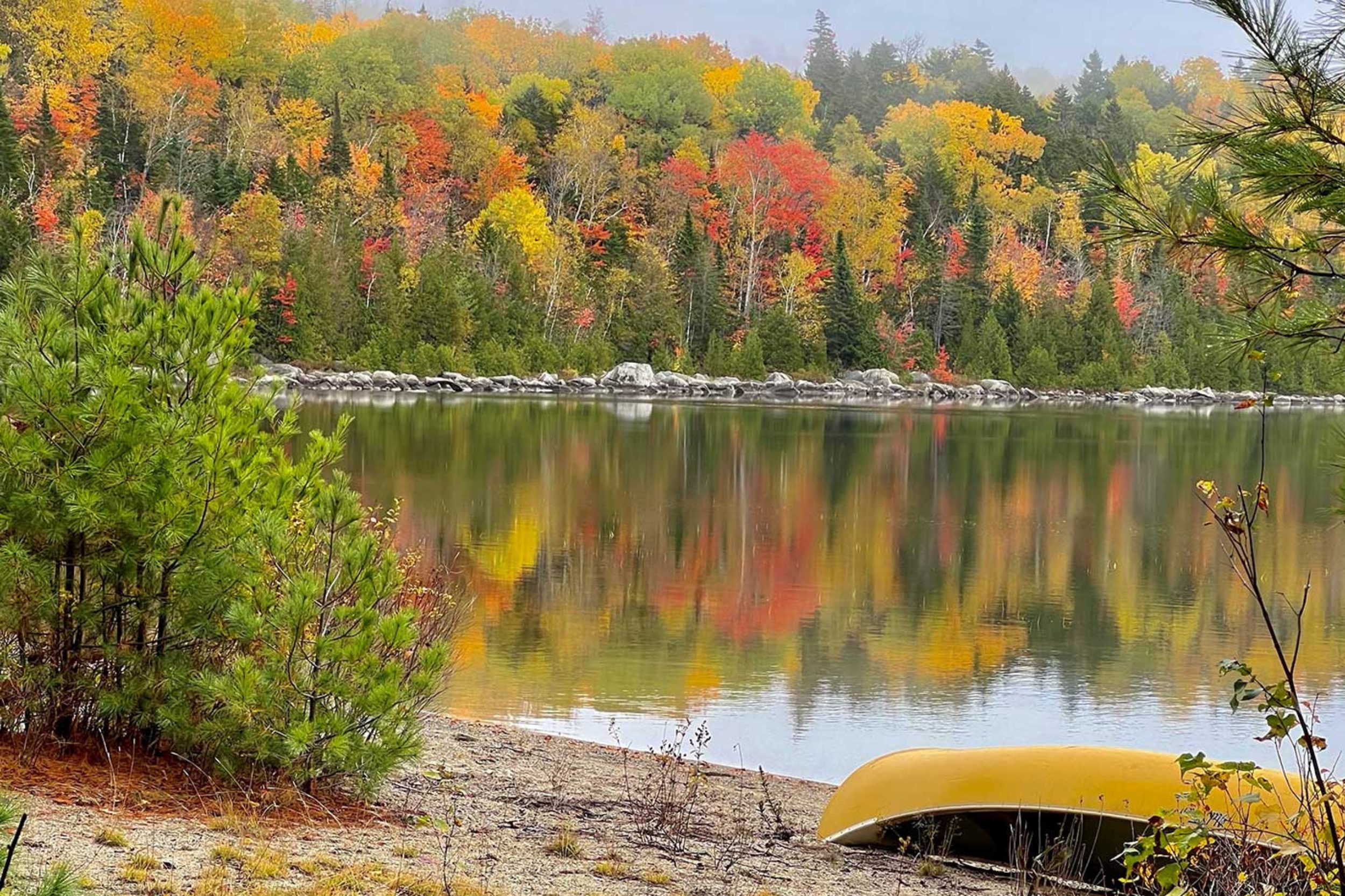 Colorful autumn trees reflecting on a calm lake with canoe on shore in Union Maine