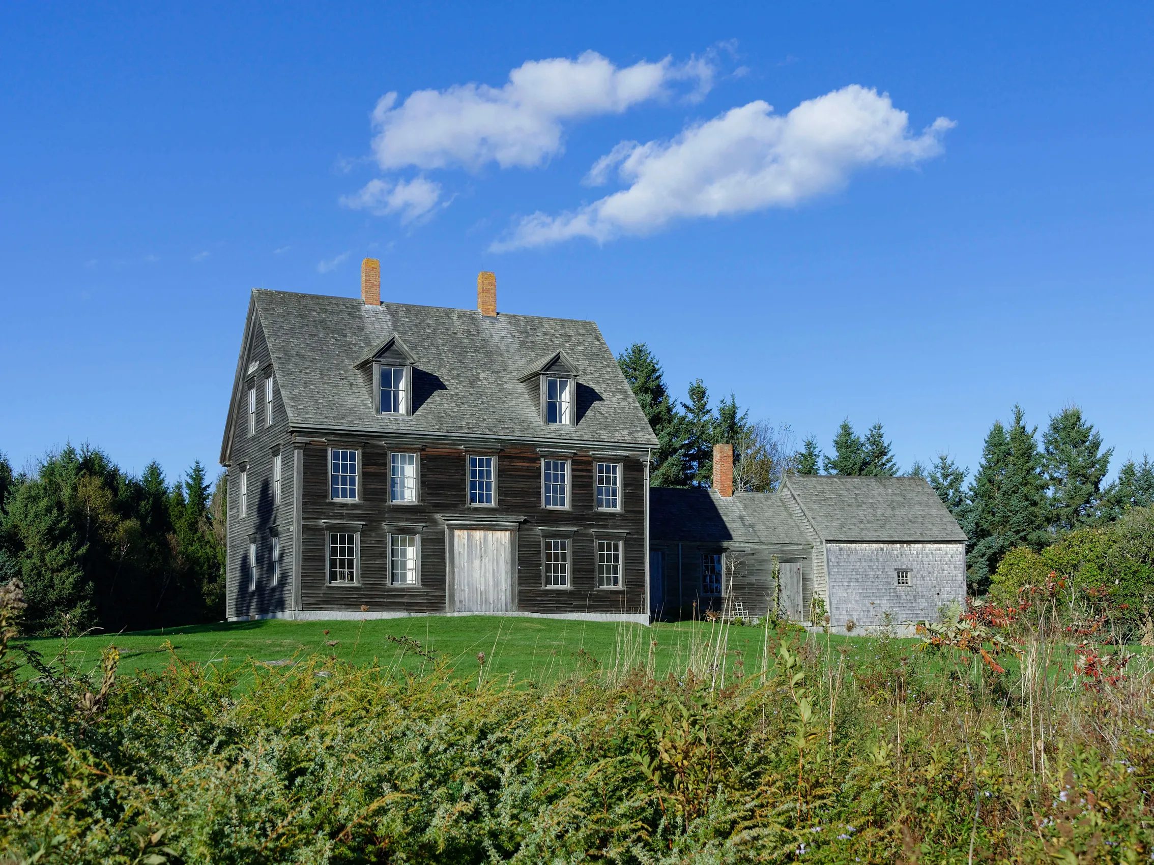 Historic wooden colonial home in rural Cushing Maine with trees and open field