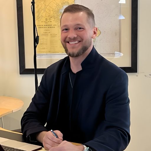 Local realtor smiling while working at a desk with a coastal Maine map in the background, representing local market knowledge and client guidance.