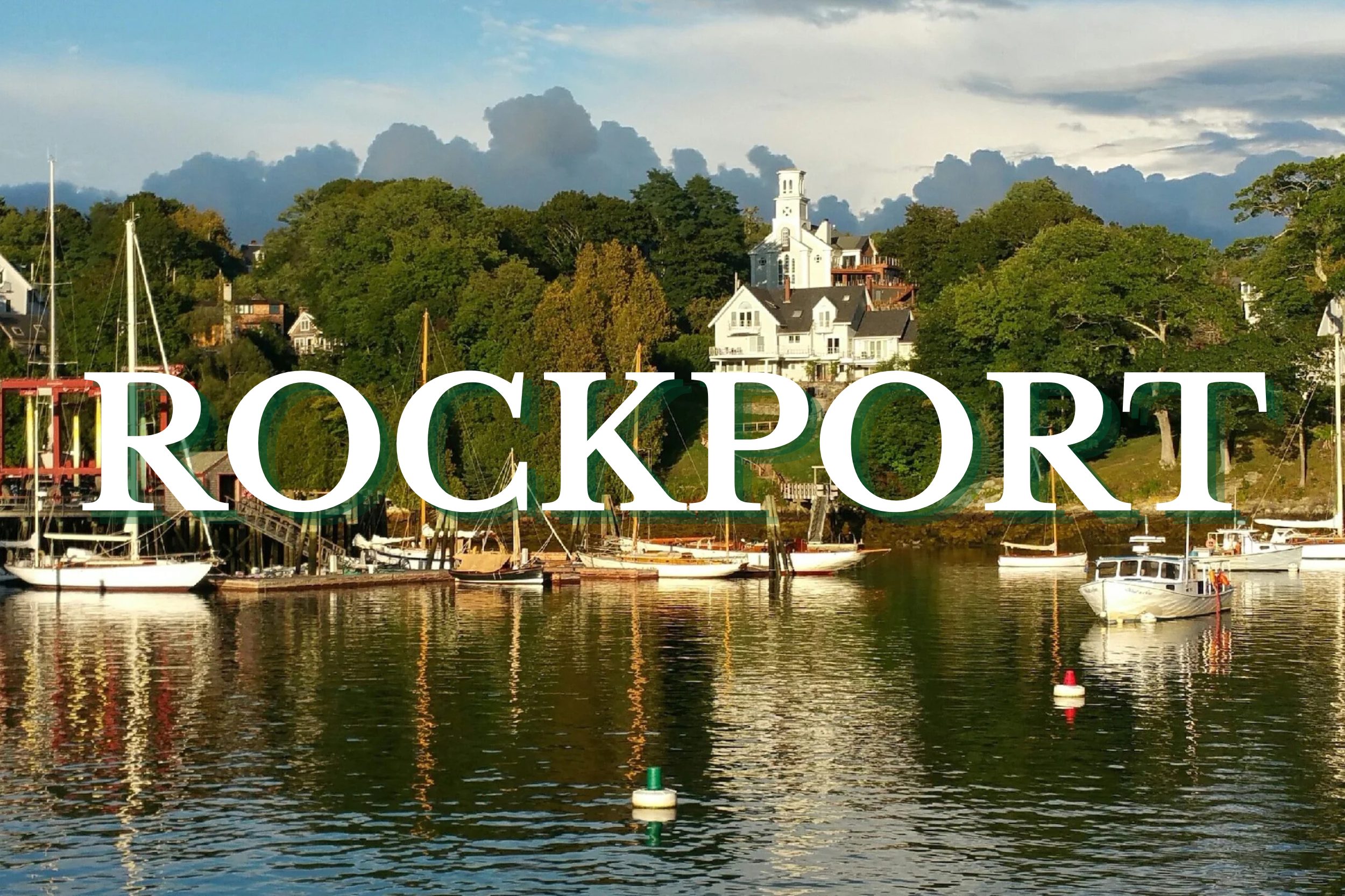 Boats resting in Rockport Harbor with waterfront homes and trees in Rockport, Maine