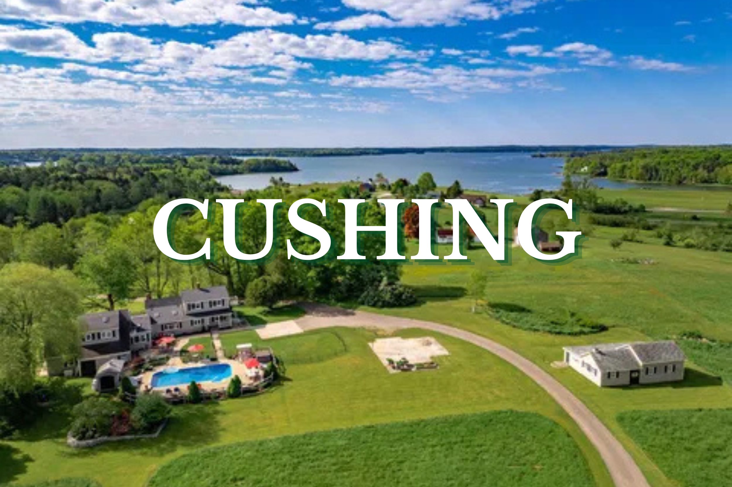 Aerial view of waterfront homes, open green fields, and coastal landscape in Cushing, Maine