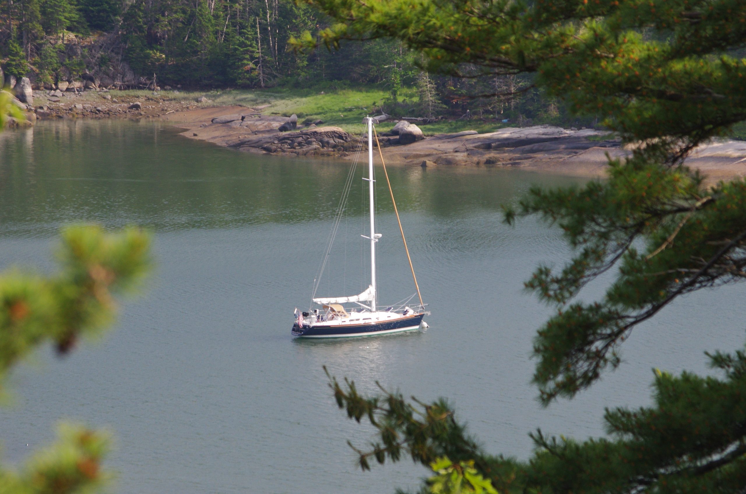 Sailboat anchored in a calm coastal cove surrounded by rocky shoreline and evergreen trees in Maine