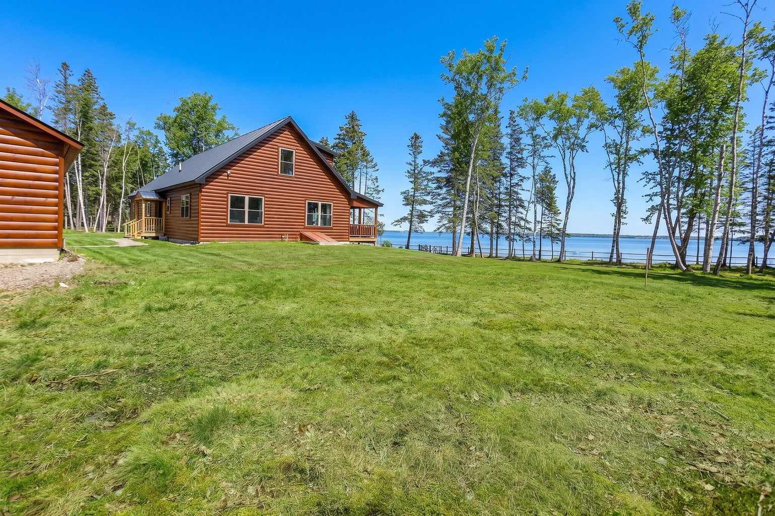 Log-style waterfront home with large grassy yard, mature trees, and water views along the Maine coast