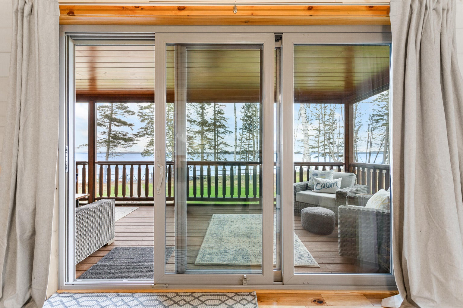 View through sliding glass doors to a covered porch overlooking a waterfront lawn and coastal Maine shoreline