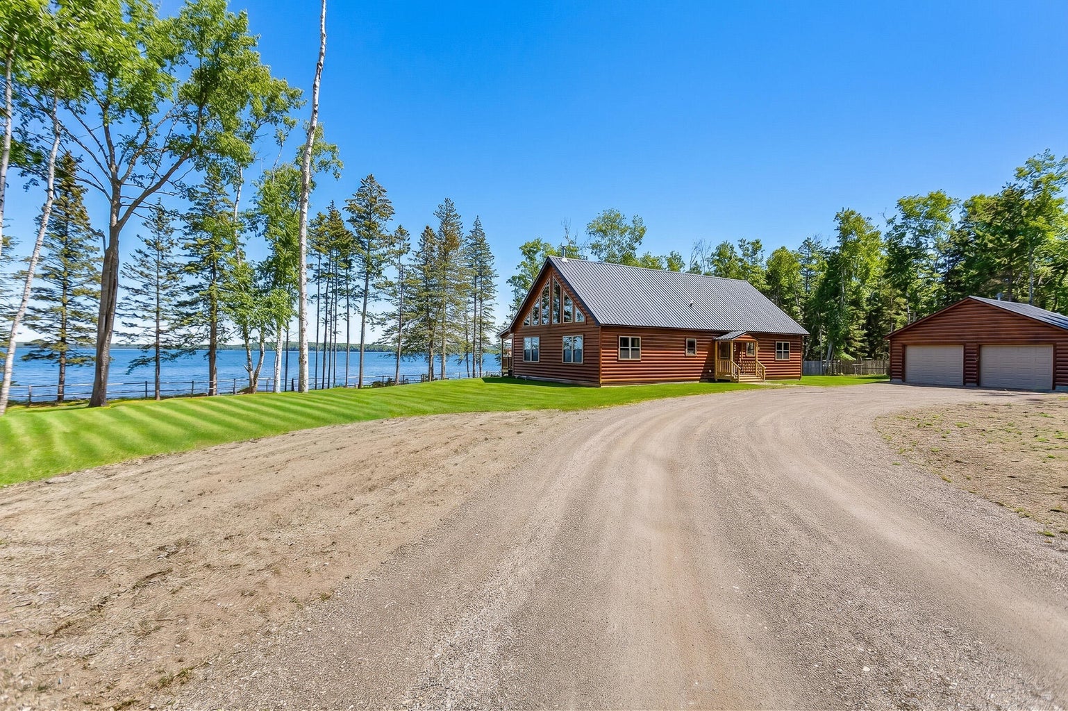 Waterfront log home with detached two-car garage, circular gravel driveway, and expansive lawn overlooking the Maine coast