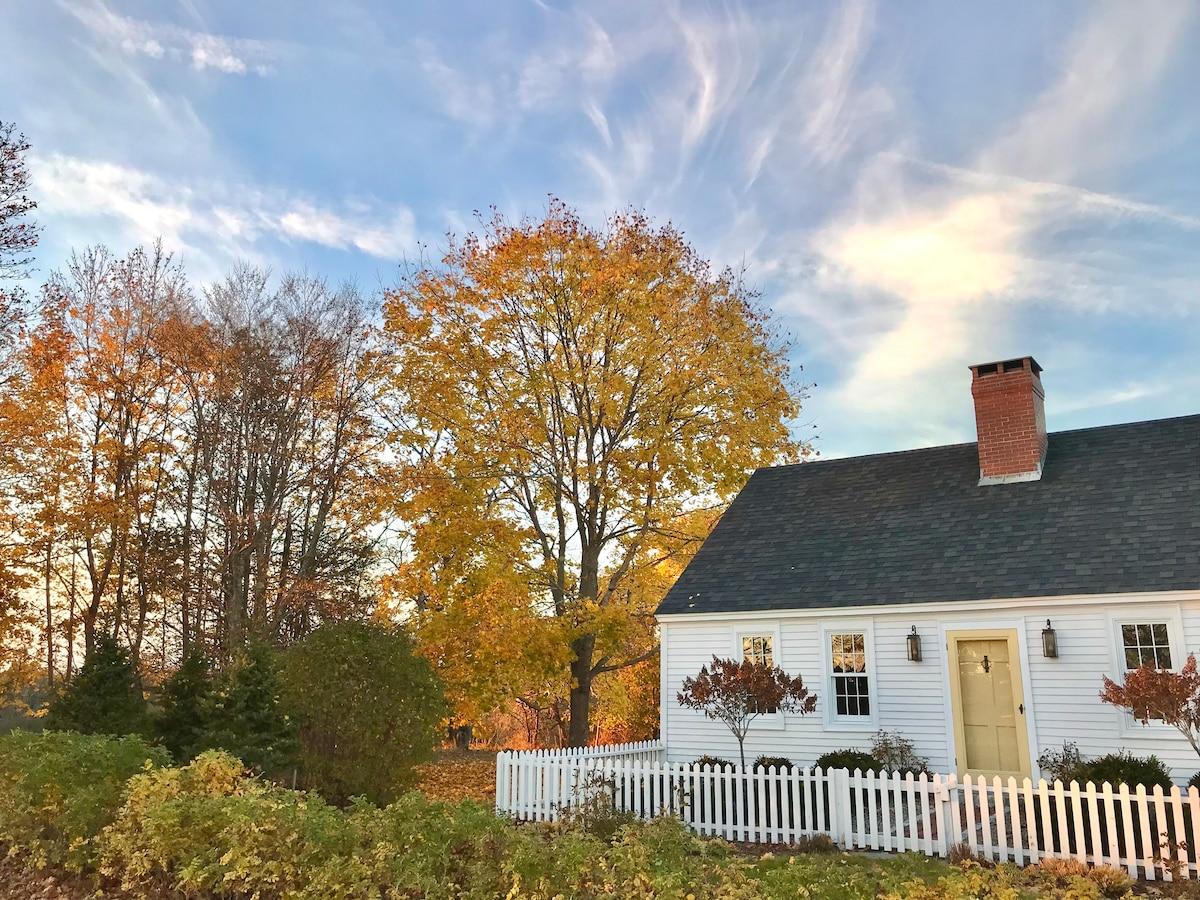White cottage with a picket fence surrounded by colorful fall foliage in Maine